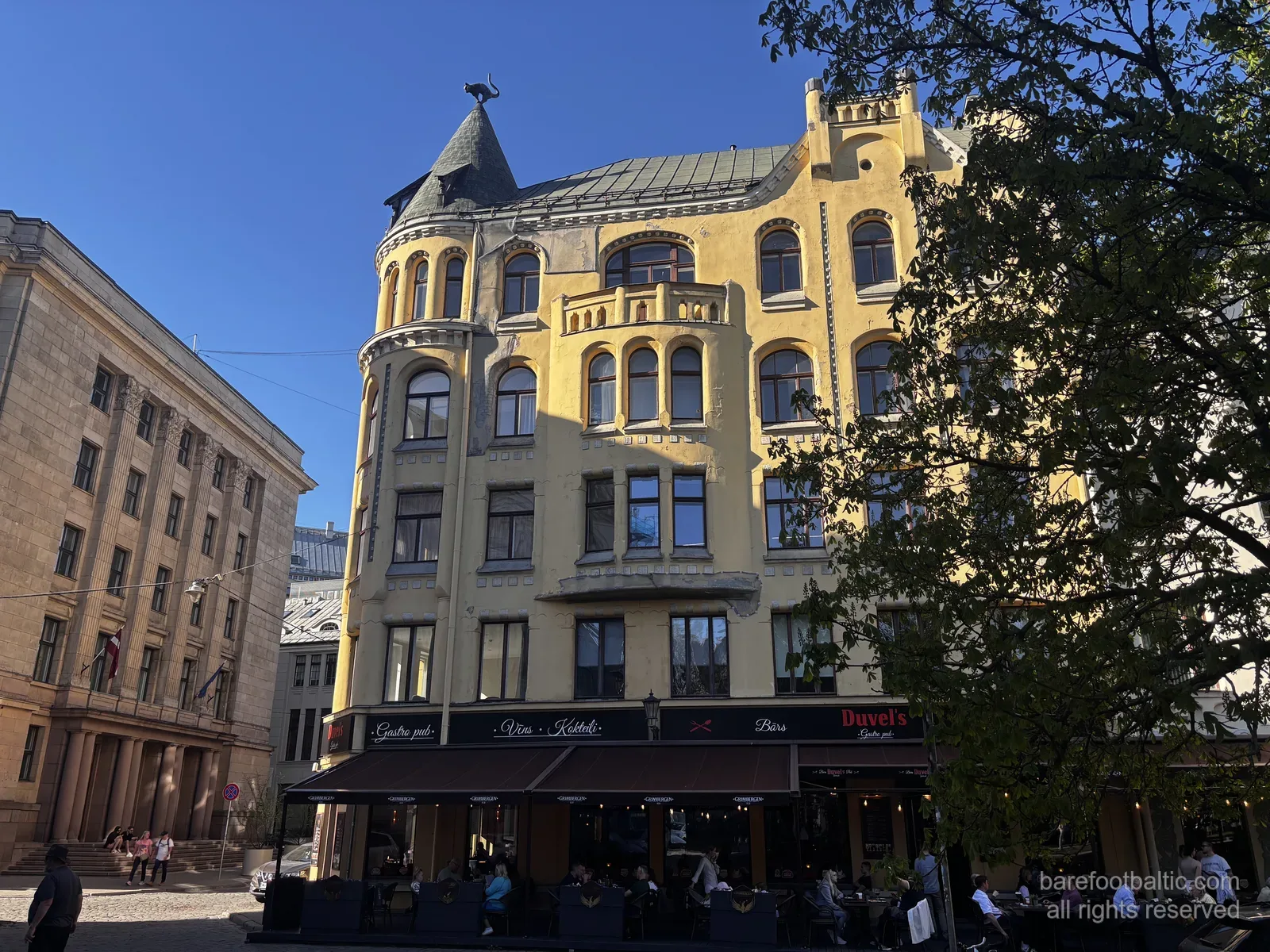 Koci Dom (Kaķu nams) przy Meistaru iela na ryskiej Starówce, z żółtą fasadą w stylu Art Nouveau i brązowym kotem na narożnej wieżyczce, Łotwa.
