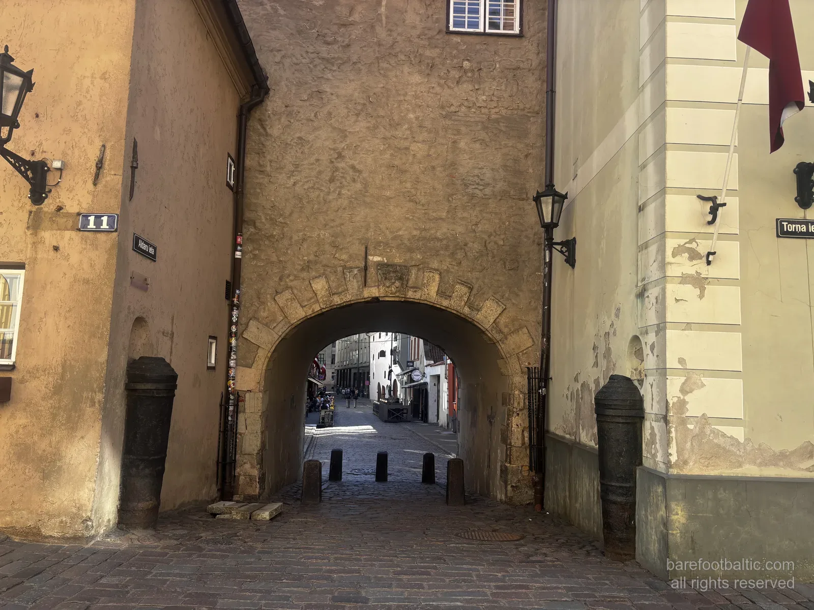 Brama Szwedzka (Zviedru vārti) przy Torņa iela na Starym Mieście w Rydze na Łotwie, kamienny łuk między dwoma żółtymi budynkami.