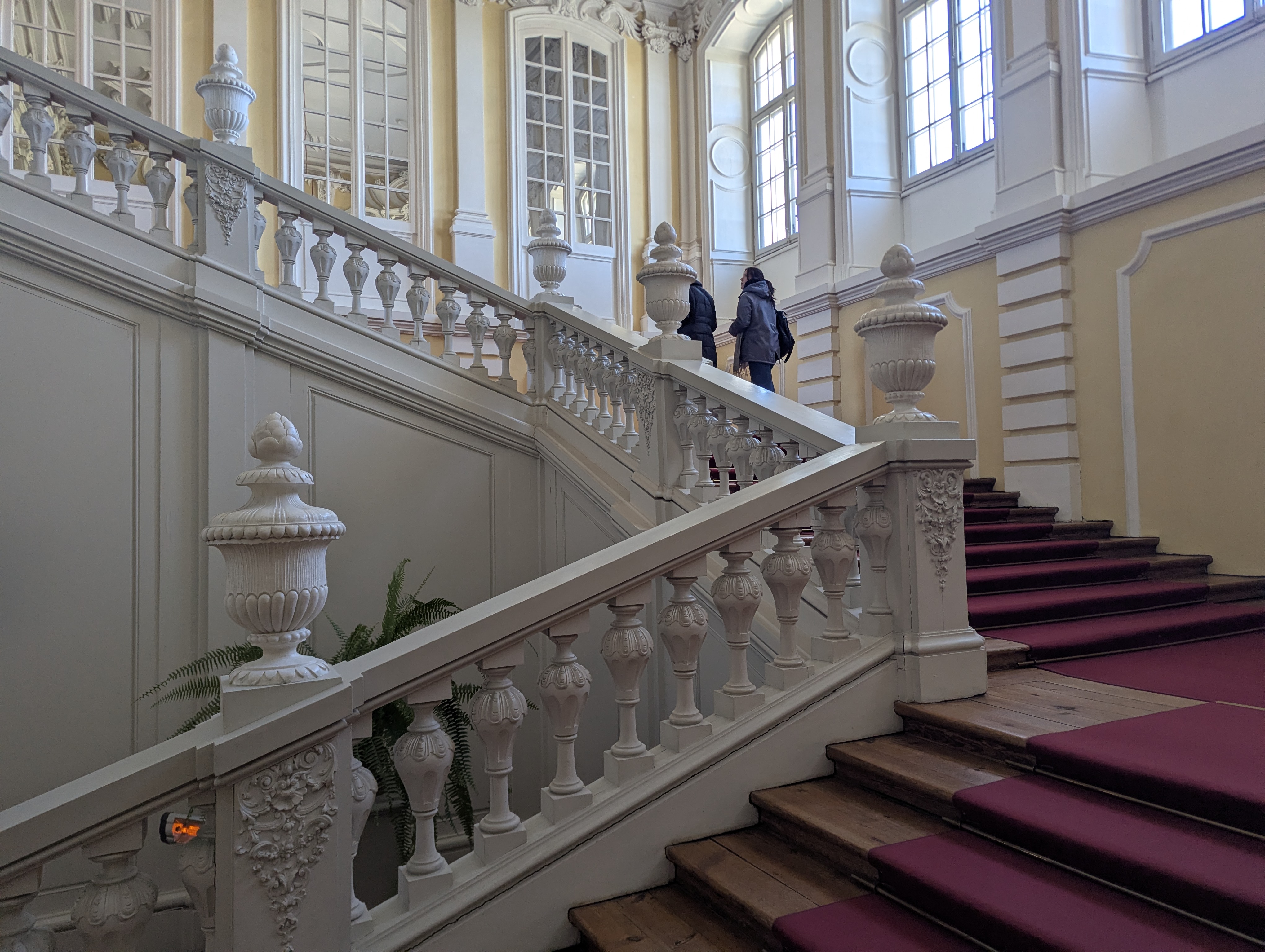 Reprezentacyjna klatka schodowa Pałacu Rundāle z barokowymi balustradami z białej sztukaterii i bordowym chodnikiem