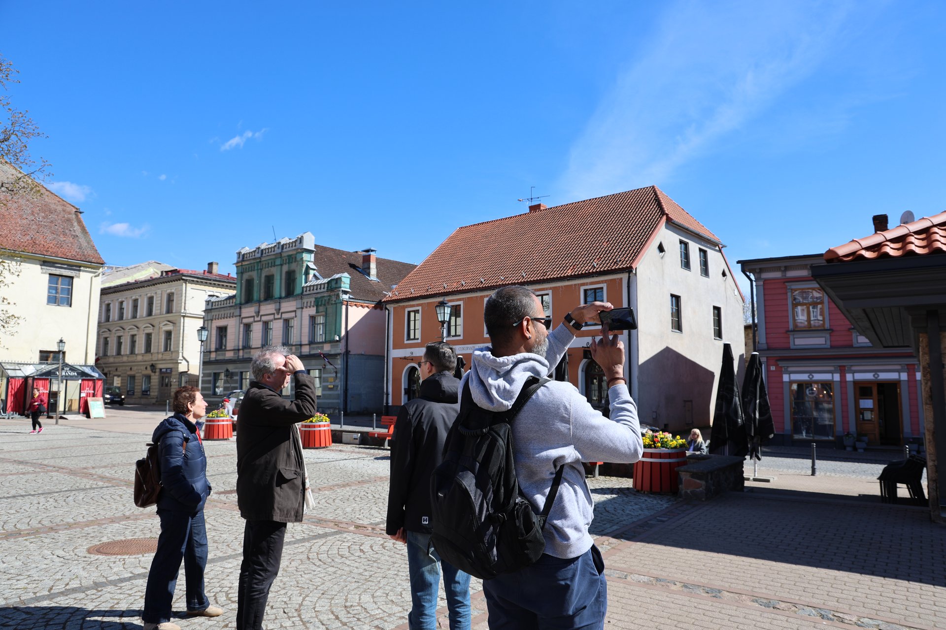 Grupa wycieczkowa fotografująca zabytkowe fasady na rynku starego miasta Cēsis